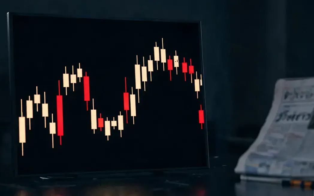 暗い取引端末に浮かぶ金と朱のローソク足の光